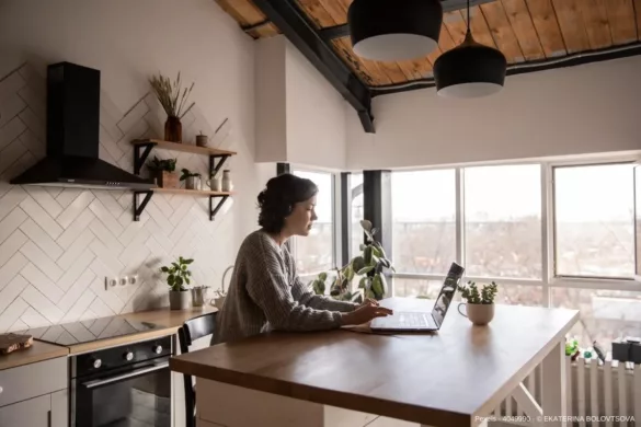 Frau sitzt in einer ordentlichen Wohnung an einem Laptop in der Küche - In diesem Beitrag erfahren Sie wissenswerte Infos darüber, wie Ordnung in der Wohnung die mentale Gesundheit stärken kann.